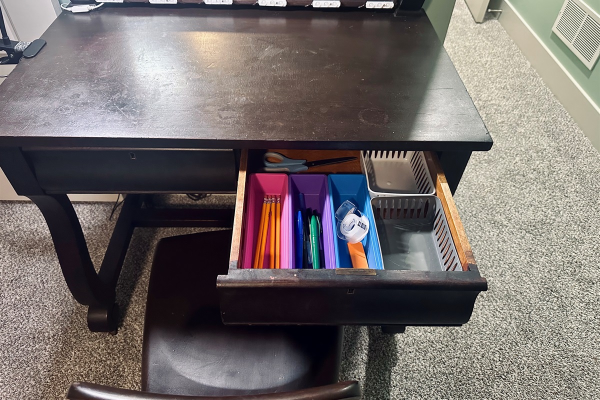 Primary suite desk drawer stocked with essential office supplies including pens, pencils, tape, and scissors for guest use.