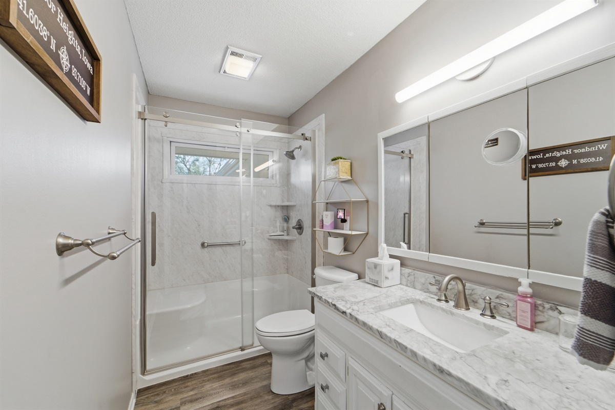Bathroom 1, is next to the kitchen on the main floor and is equipped with a large walk-in shower, granite countertop vanity, and lots of plush towels.