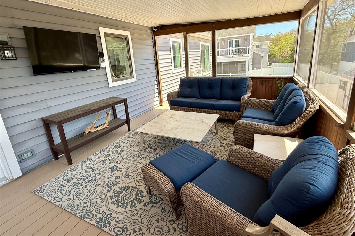 Enjoy ultimate relaxation on this elegant screened-in porch. Featuring comfortable wicker seating with plush blue cushions and a wall-mounted TV, it's the perfect luxury space for unwinding.