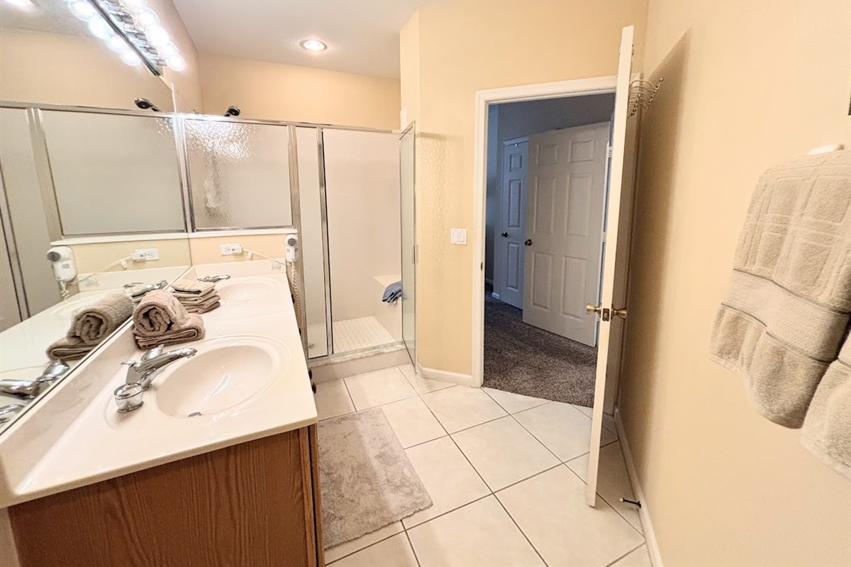 Bright bathroom with spacious vanity, large mirror, tile flooring, and a walk-in shower with glass doors.