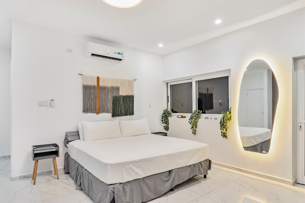 Primary bedroom detail: King bed with LED mirror and greenery on window ledge