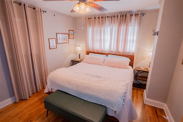 King bedroom featuring a wall-mounted smart TV, modern lighted vanity, and cozy bedding. Bright, functional setup for relaxing or getting ready.