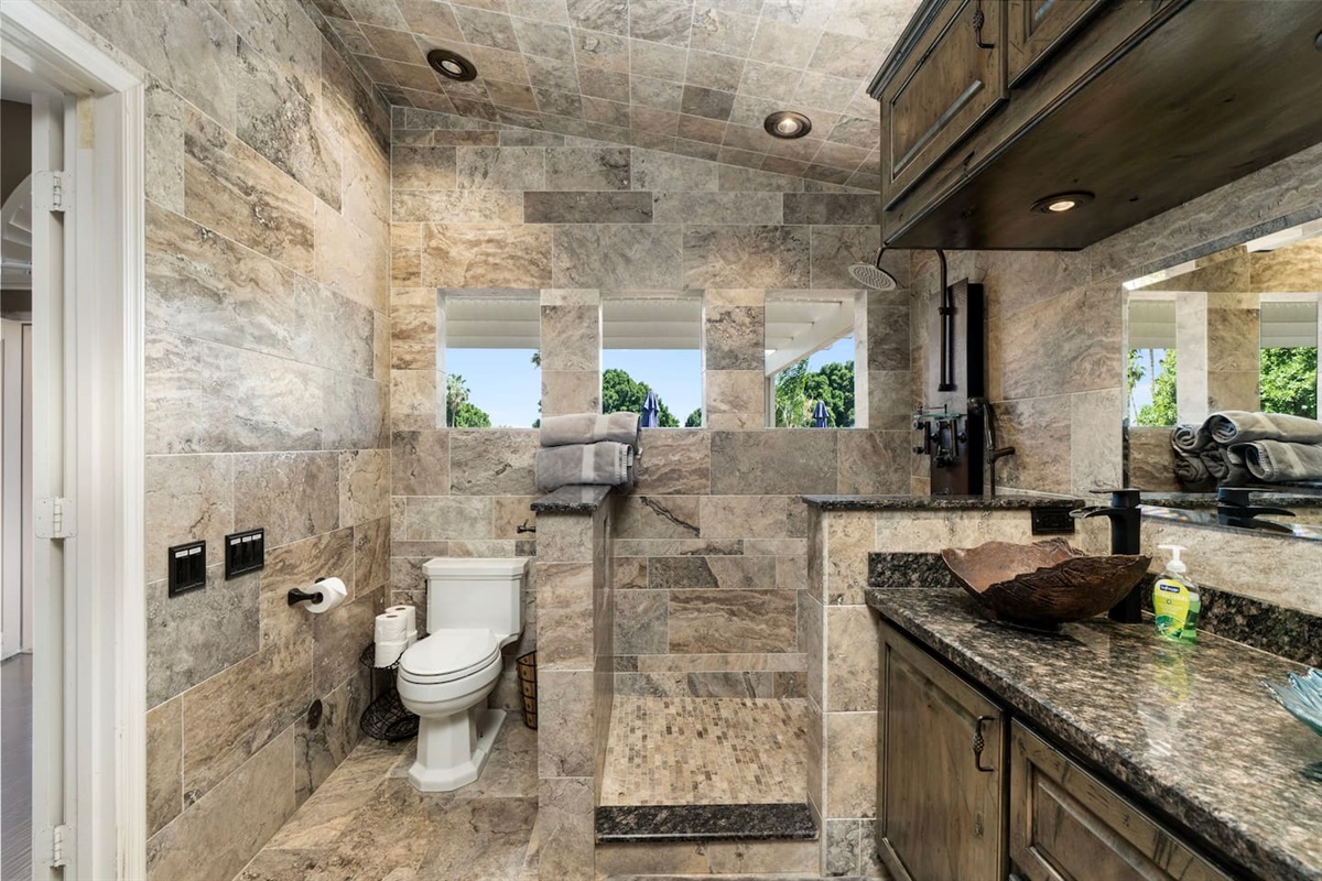 The open walk-in shower is a showstopper — fully tiled in natural travertine with open windows that bring in light and air, making every shower feel like an outdoor escape.