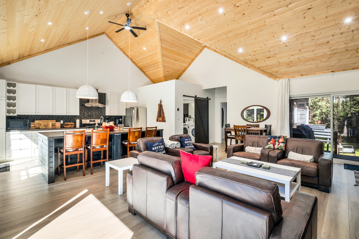 Come together in the bright, open-concept living space, where the kitchen, dining area, and lounge flow naturally under a warm vaulted wood ceiling.