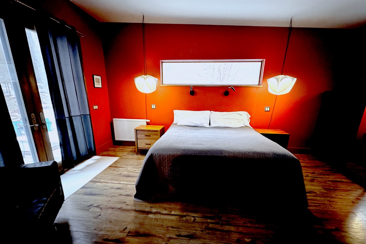 The sophisticated primary suite features a King bed and statement designer lighting. Enjoy direct, private access to the expansive deck through oversized glass doors, perfectly positioned to blend modern comfort with the natural beauty of the Acadia border