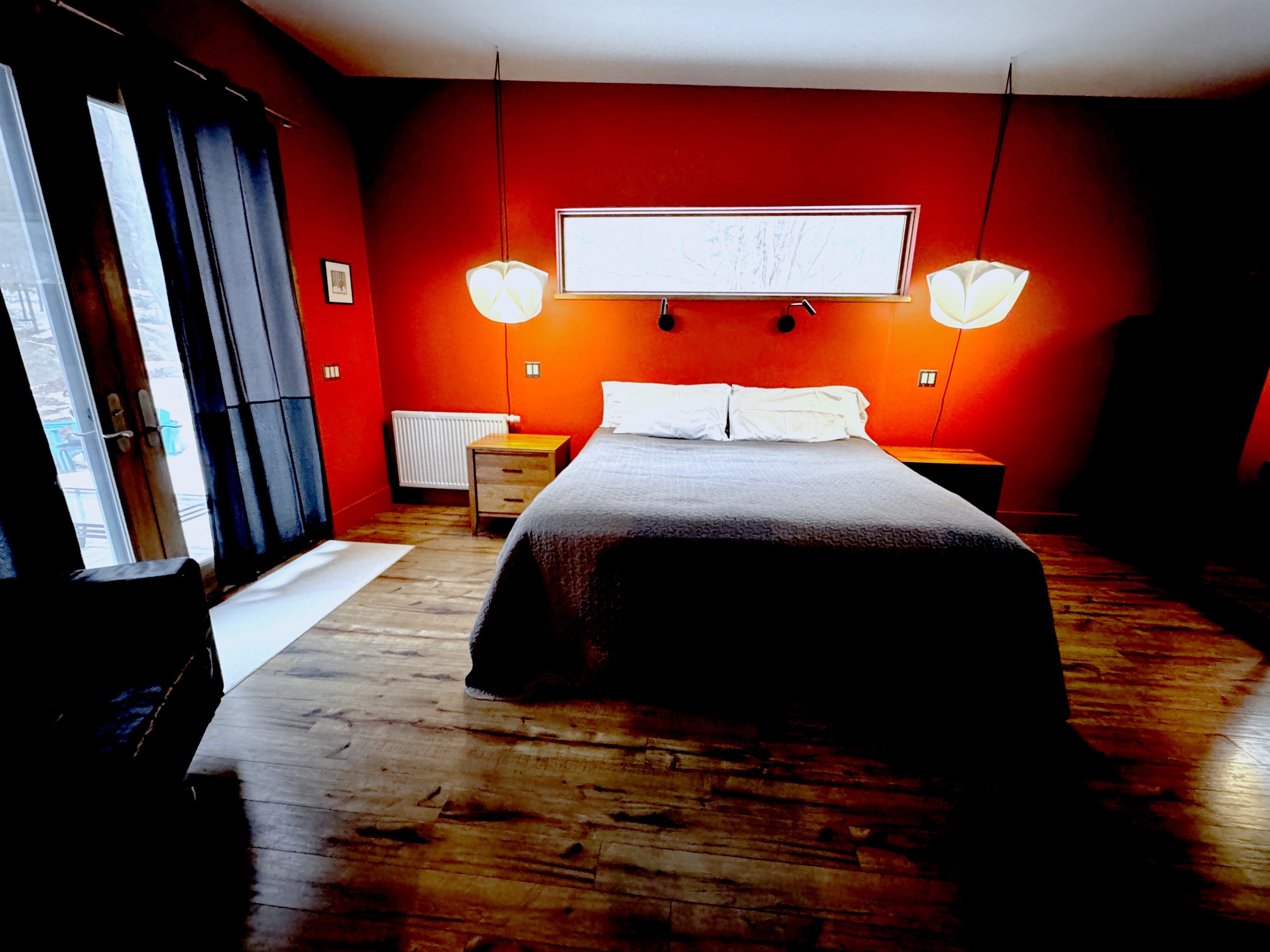 The sophisticated primary suite features a King bed and statement designer lighting. Enjoy direct, private access to the expansive deck through oversized glass doors, perfectly positioned to blend modern comfort with the natural beauty of the Acadia border