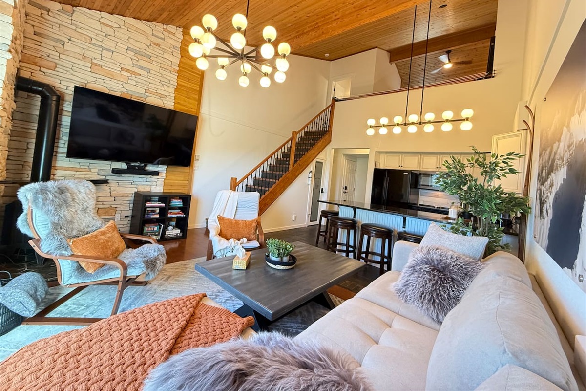 Bright open-concept living area with soaring cedar ceilings, a stone fireplace, and modern lodge lighting — the perfect place to unwind after exploring Kimberley’s mountain adventures.