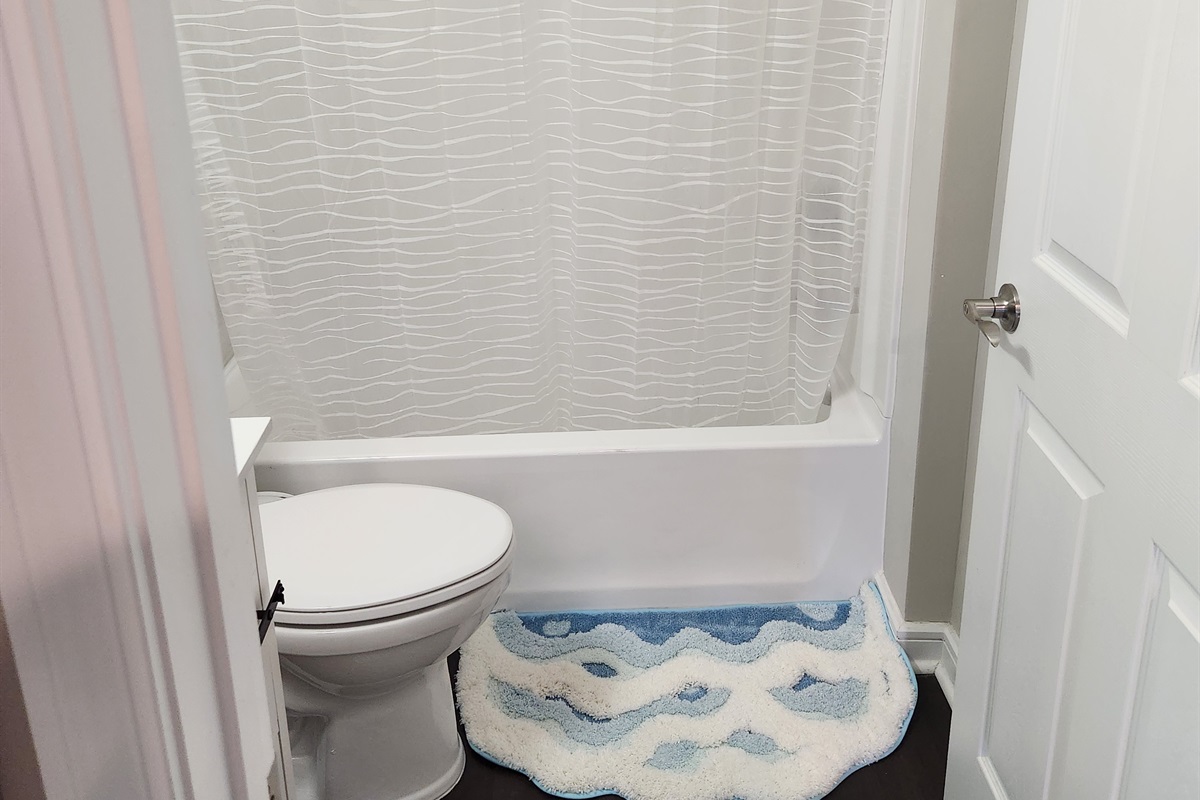 Enjoy a clean and modern bathroom space complete with a wave-patterned shower curtain, dark wood flooring, and a contemporary vanity with plenty of storage.