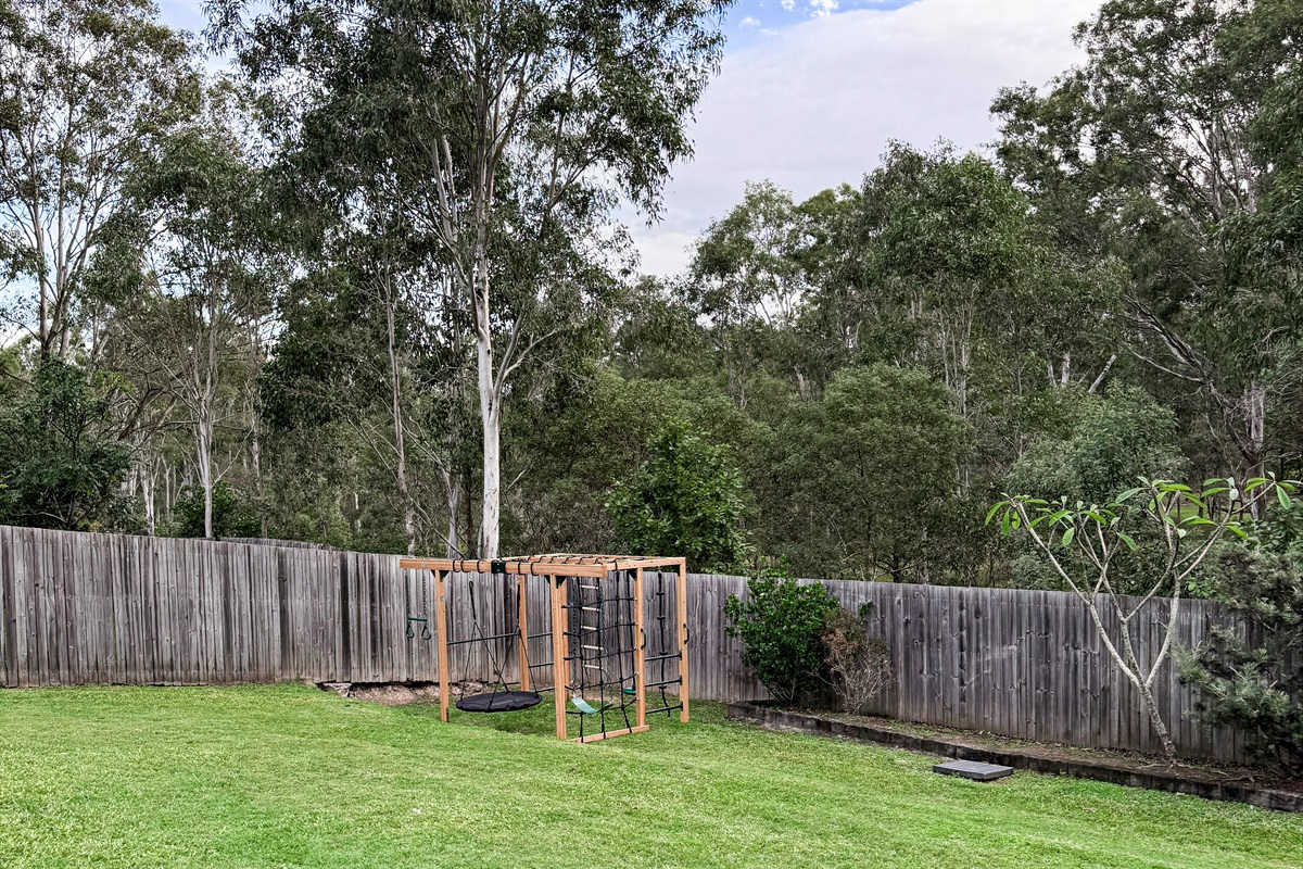 The jungle gym sits inside the fenced backyard, with swings, climbing sections and lawn space around the play structure.