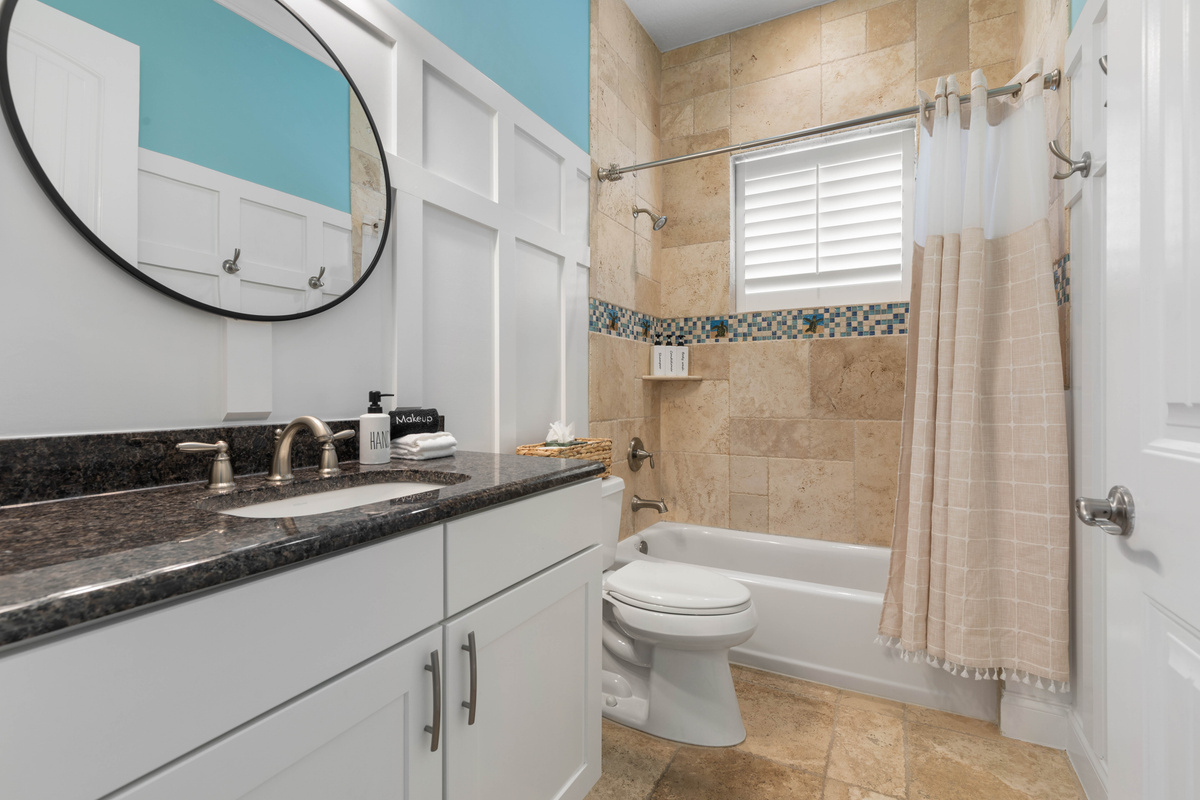 Turquoise bath with a granite vanity, a round mirror and a tub-shower combo, an easy setup for bath time with kids.