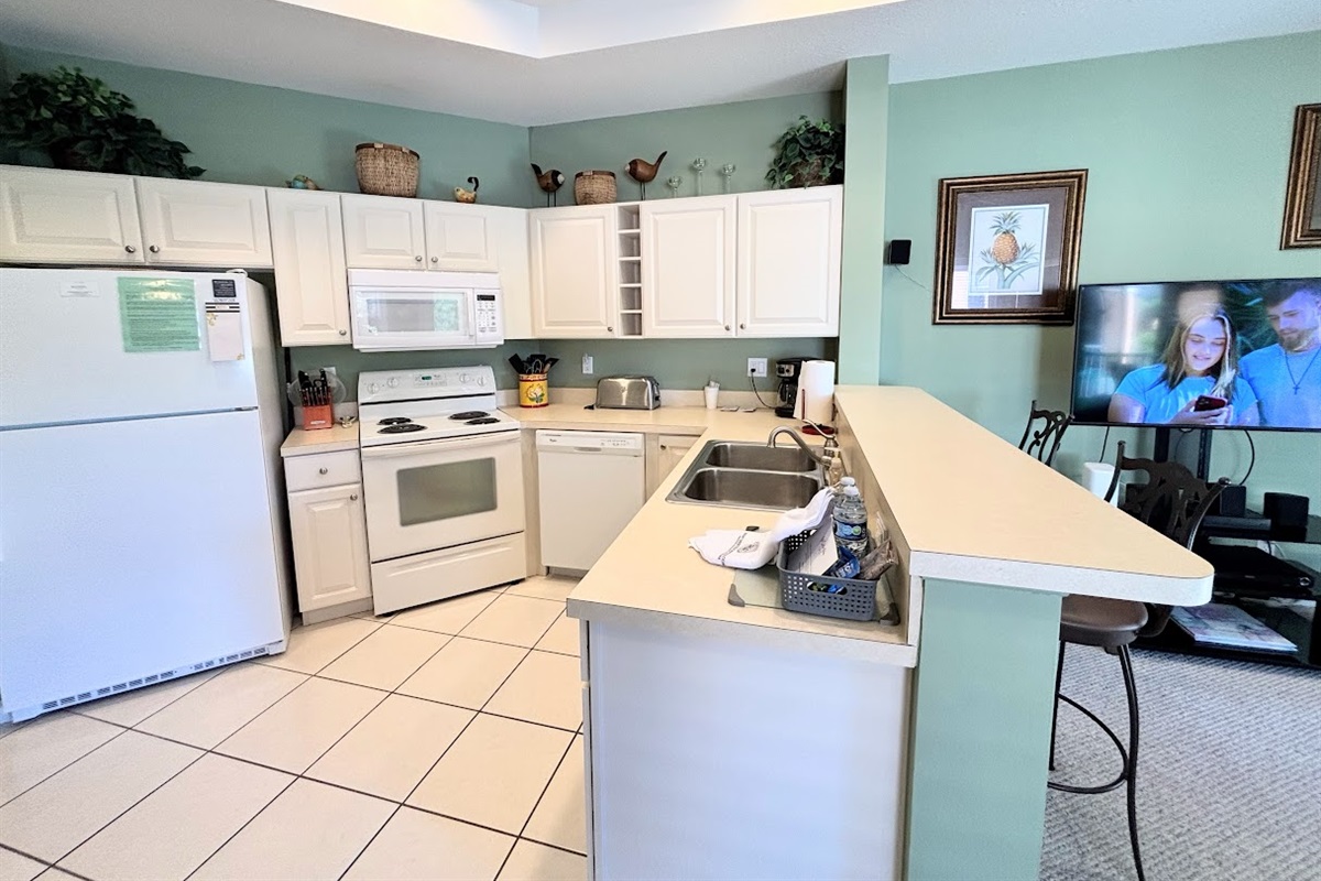 Fully equipped kitchen with full-size appliances, breakfast bar seating, and an open view into the living area.