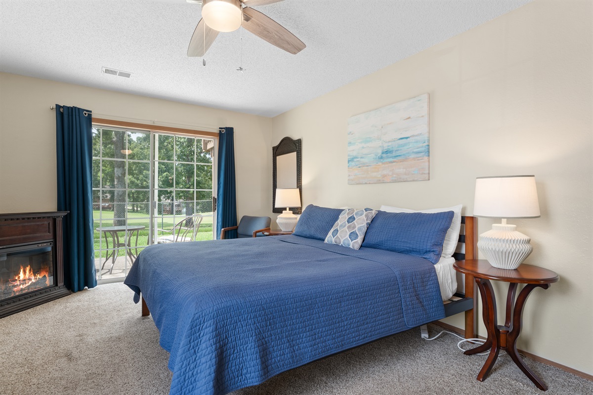 Primary bedroom with king bed, electric fireplace, and sliding door to patio.