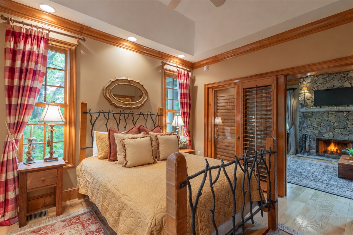 The cozy main-level queen bedroom offers warm mountain charm, wooded views, and easy access to the inviting living room with its stunning stone fireplace just steps away.