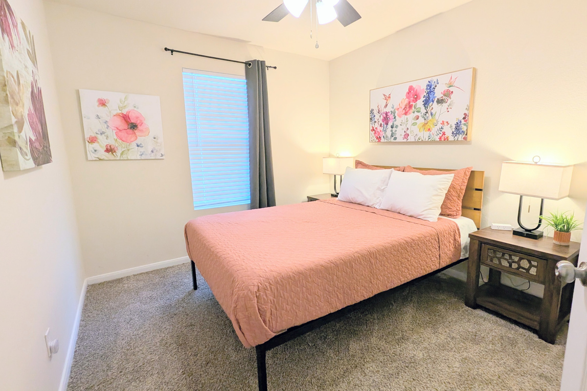This bedroom features a comfortable queen bed with sheets, blanket, quilt and plush pillows. Convenient charging ports, room darkening curtains and blinds, alarm clock, and ceiling fan are provided. 
