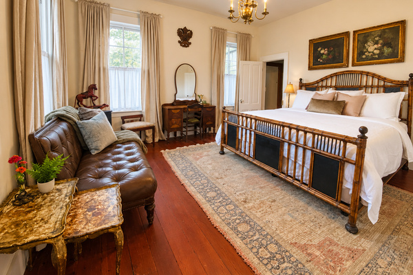 Boudoir de Bouge, our first-floor primary suite: plush bedding, room-darkening curtains, a Ralph Lauren leather sofa, and an antique vanity. An adjoining dressing room leads to your private en suite bath. 