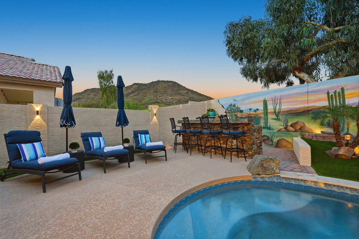 Private pool at dusk with lounge seating, outdoor bar, desert mural, and mountain views for relaxed evening downtime.