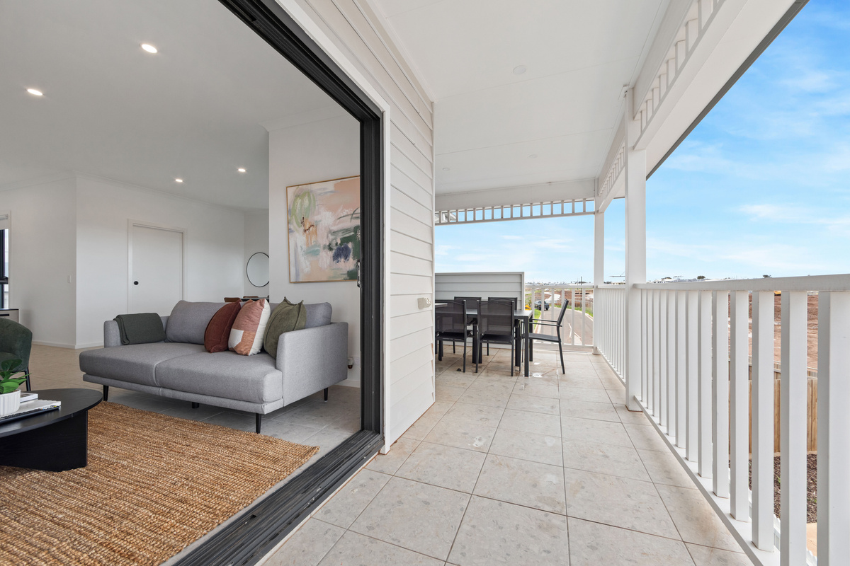 View from the balcony through the wide sliding doors into the upstairs lounge, with sofa, dining table and easy indoor-outdoor flow.