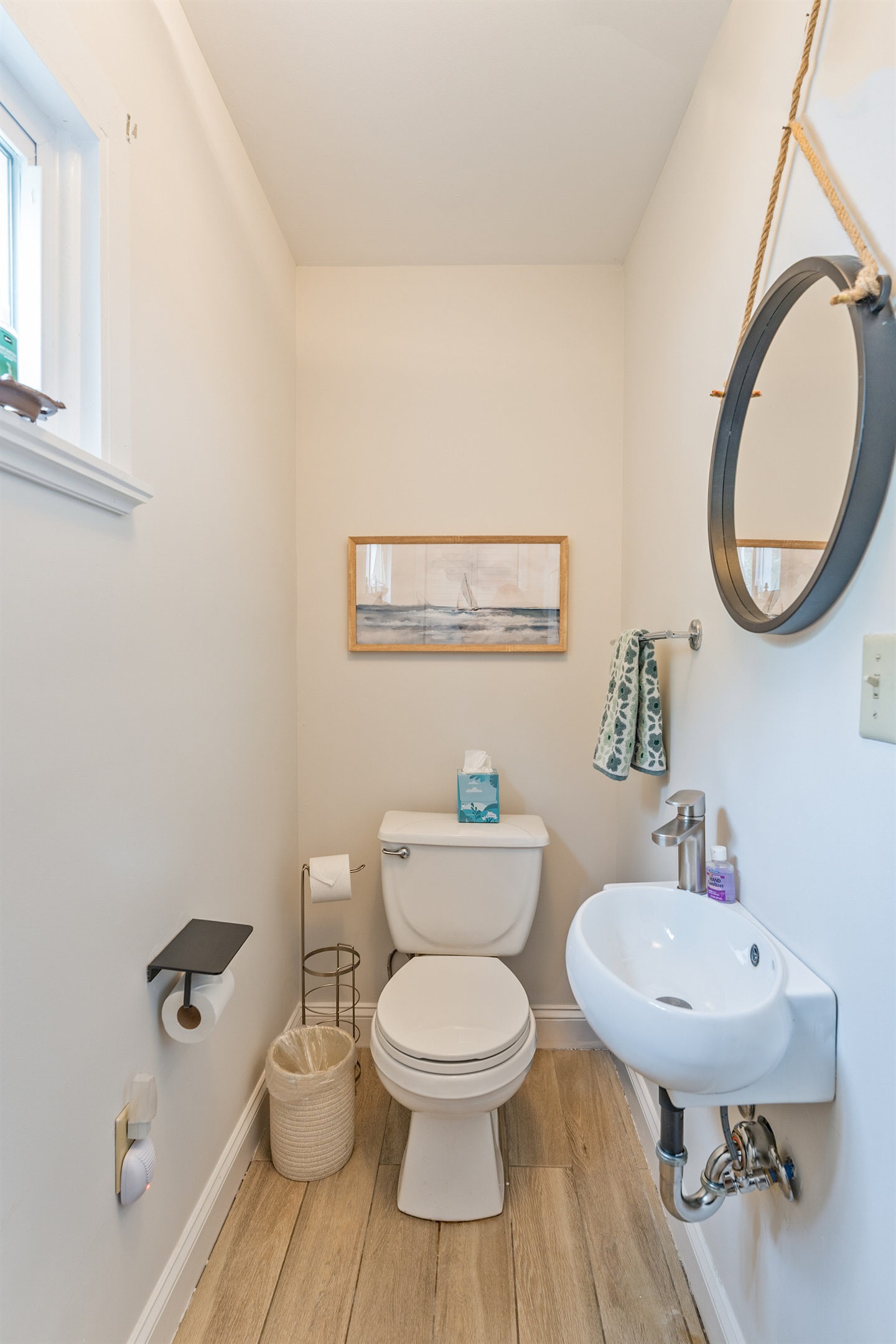 Bright and stylish half bath featuring nautical artwork, wood-style floors, and a sleek modern sink—perfect for guest convenience! Just off the living room on the main floor