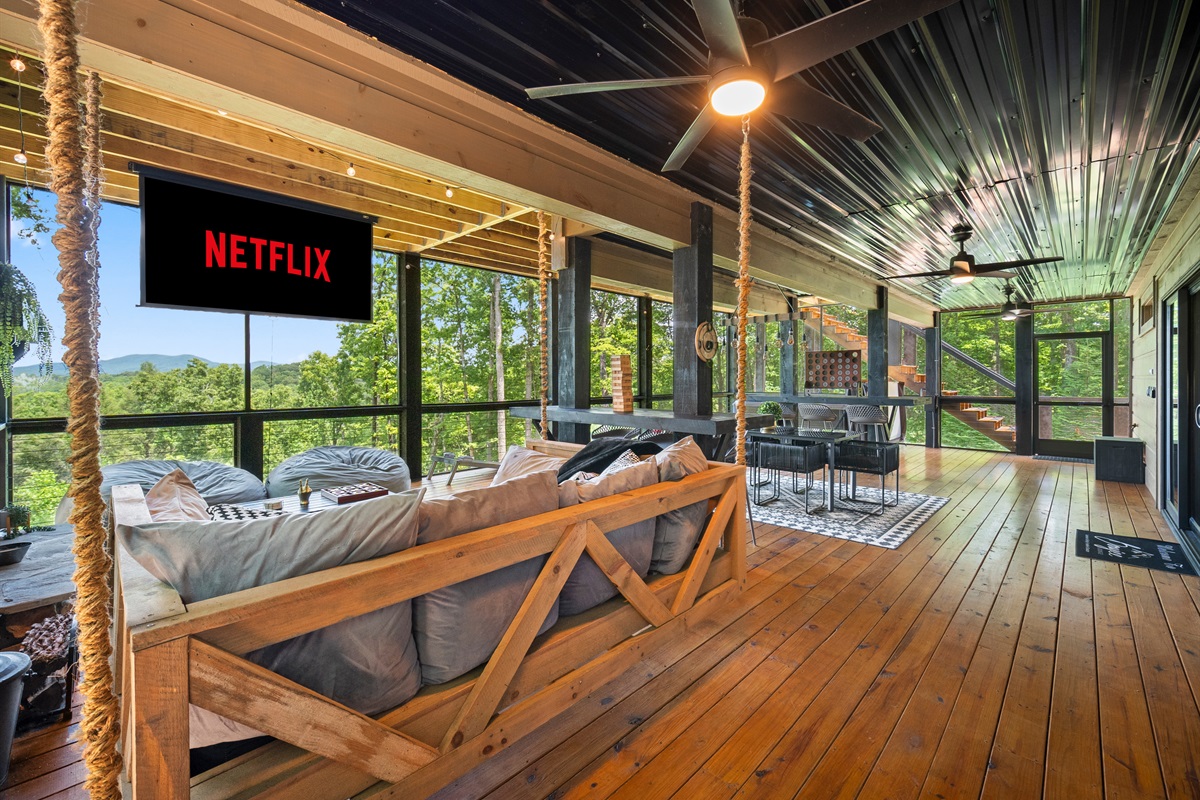 This spacious screened-in porch combines modern comfort with rustic charm, queen-size sofa bed, movie projector, lush greenery, and mountain views.