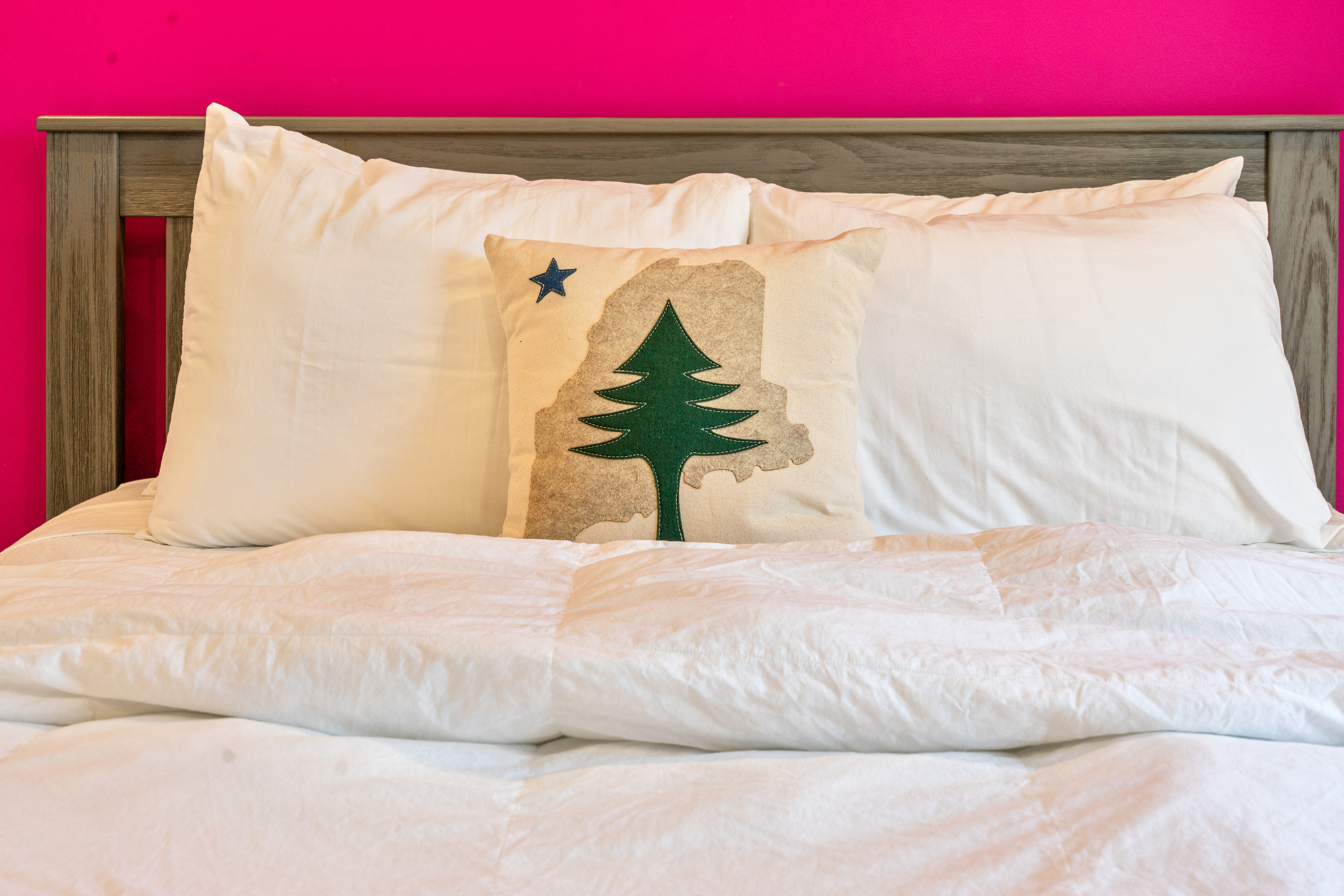 A local nod to the pine tree state. This guest bedroom features a Queen bed with a textured wood headboard, crisp white linens, and a custom accent pillow. A bright, comfortable retreat just steps from downtown shops and dining.