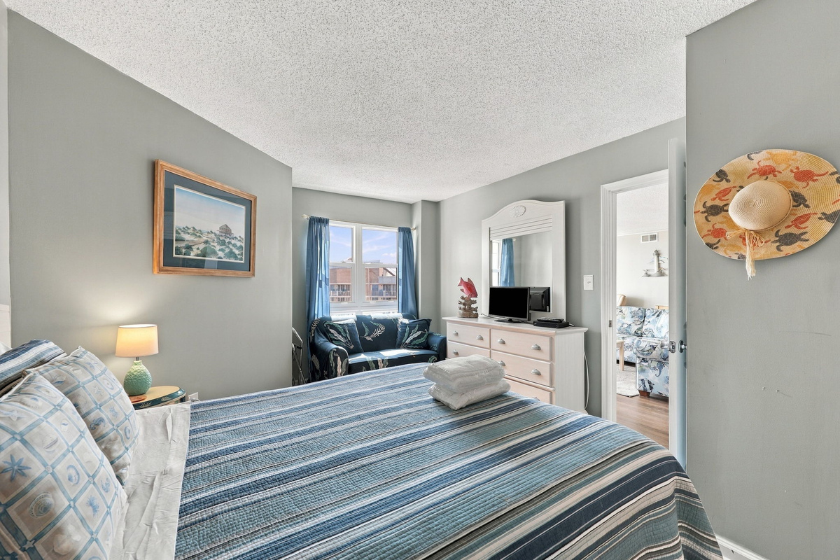 Bright, cozy master bedroom with a queen bed, coastal blue bedding, light blue walls, and a view into the attached bathroom.