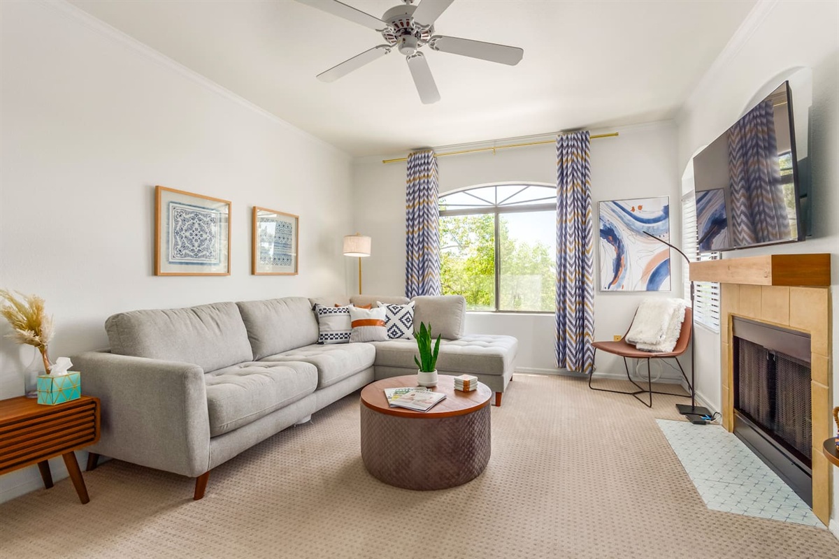 Living room with sectional seating, wall-mounted TV, fireplace, ceiling fan, and natural light from arched windows.