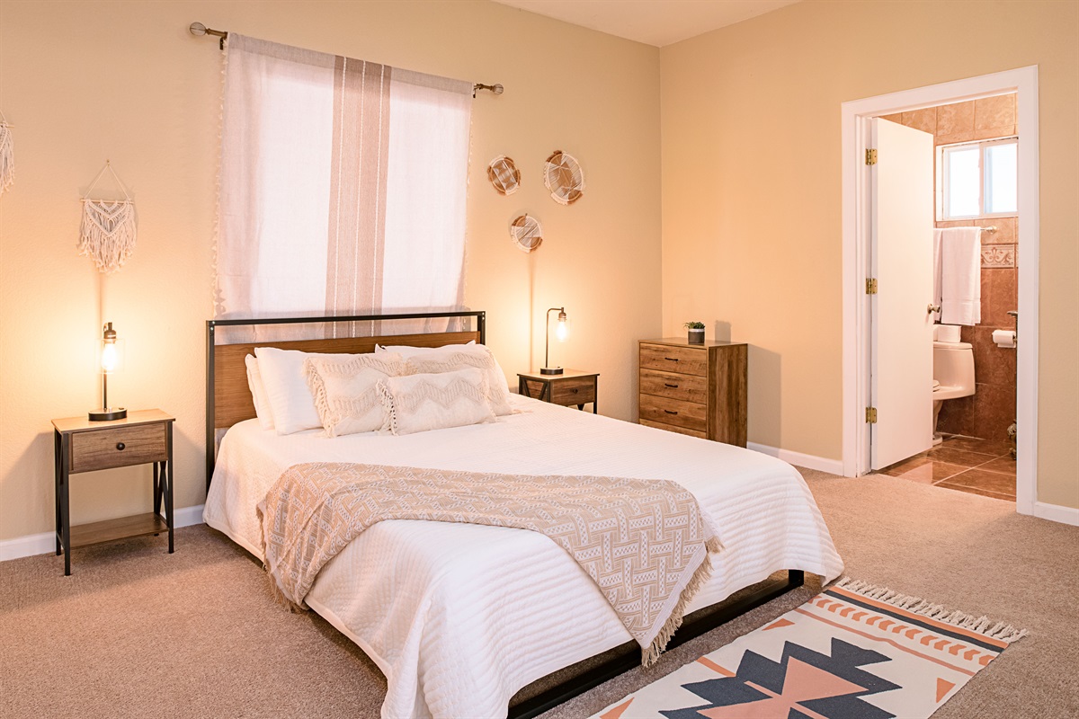 This serene bedroom blends soft earth tones, boho-chic decor, and an en-suite bath for a restful stay with comfort and style.