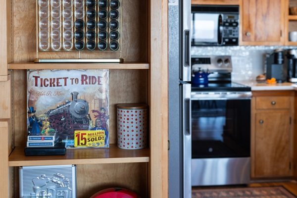 Find a selection of board and card games stored in the open shelf cabinet in the kitchen.