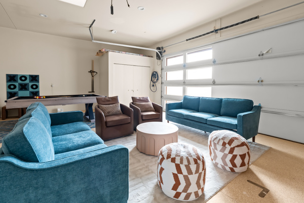 Expansive lounge setup with double plush sofas, leather armchairs, patterned poufs, and seamless access to the pool table area.