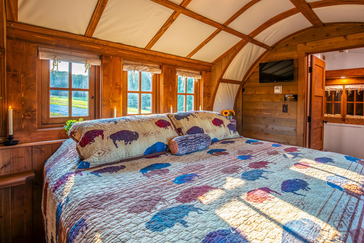King bed with warm wood walls, soft natural light, and a cozy covered wagon atmosphere.