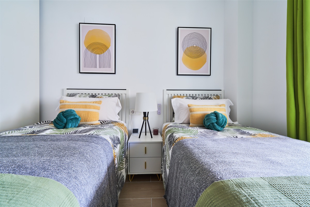 Bright and calming twin bedroom with tropical tones, soft linens, and direct access to the terrace - perfect for relaxed mornings and restful nights.