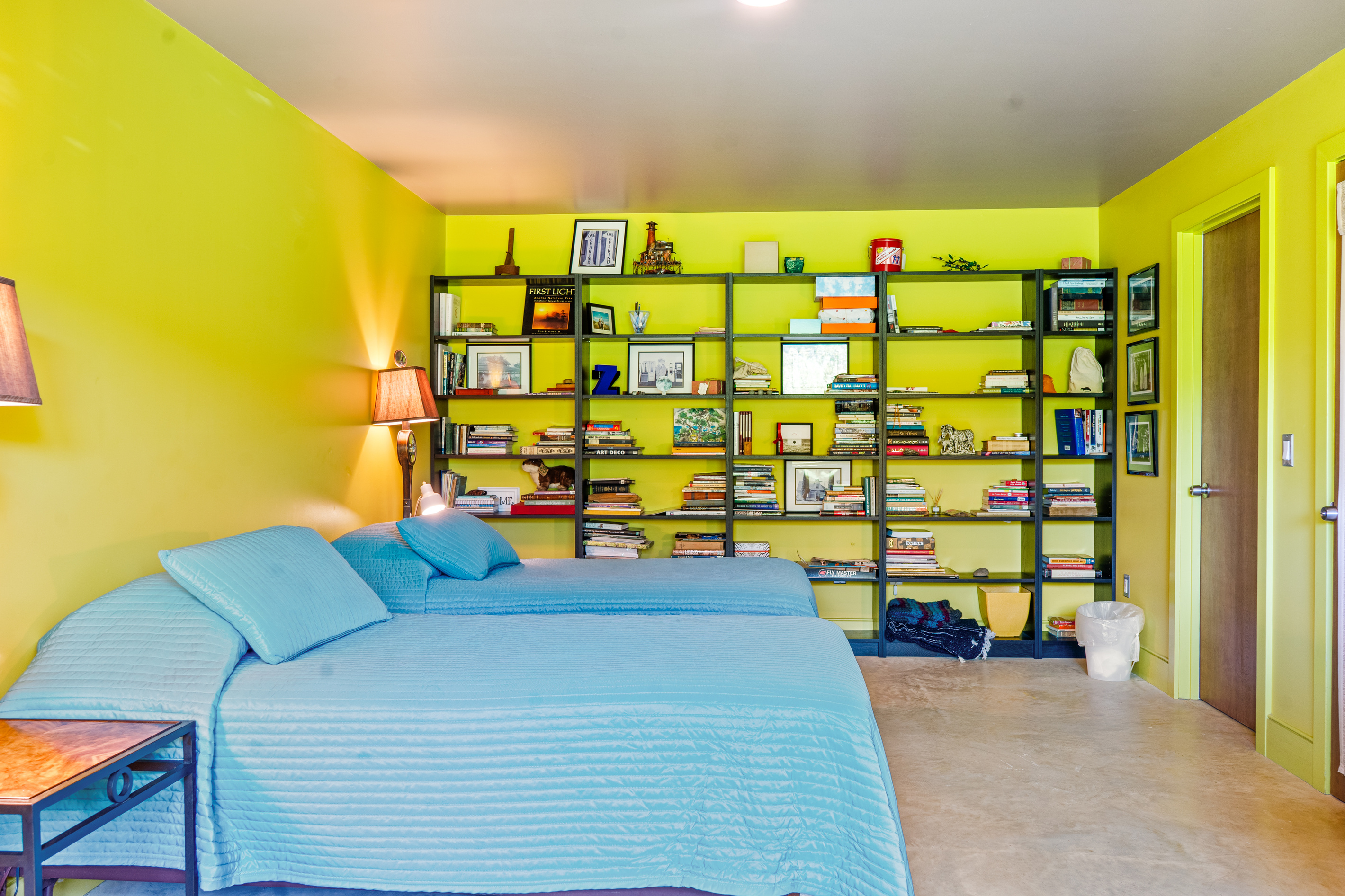 The Base Camp twin bedroom features a full wall of curated books, local literature, and games. Polished concrete floors and bright, modern design make this ground-floor sanctuary at "The Crag" ideal for post-hike downtime near Acadia.