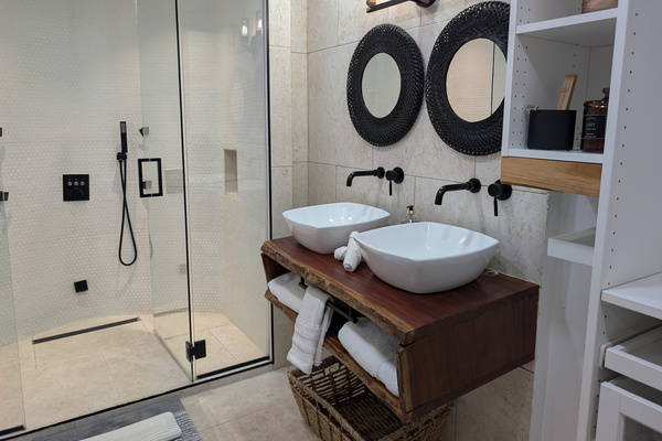 Handmade live-edge mahogany double vanity with white vessel sinks, matte black wall-mounted faucets, industrial lighting, and round black mirrors in the primary bathroom at Villa Coral in Dorado, Puerto Rico
