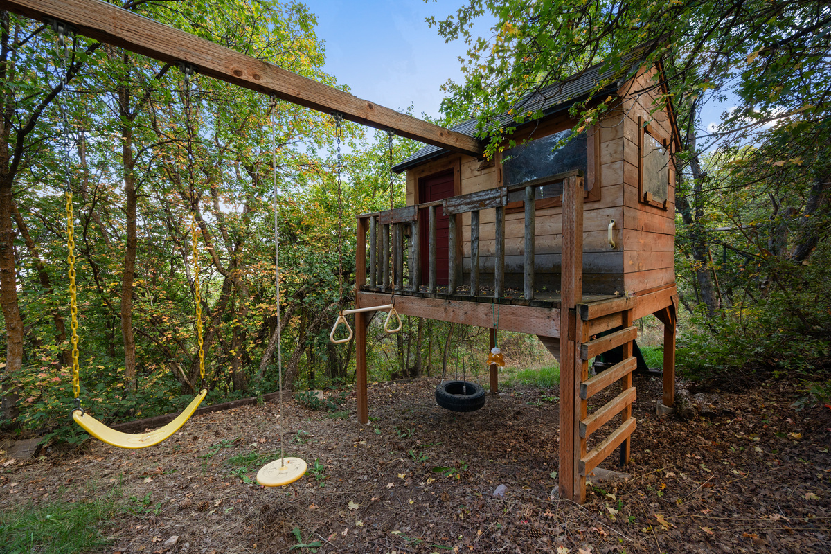 Children’s playhouse and swing set tucked into the wooded backyard.