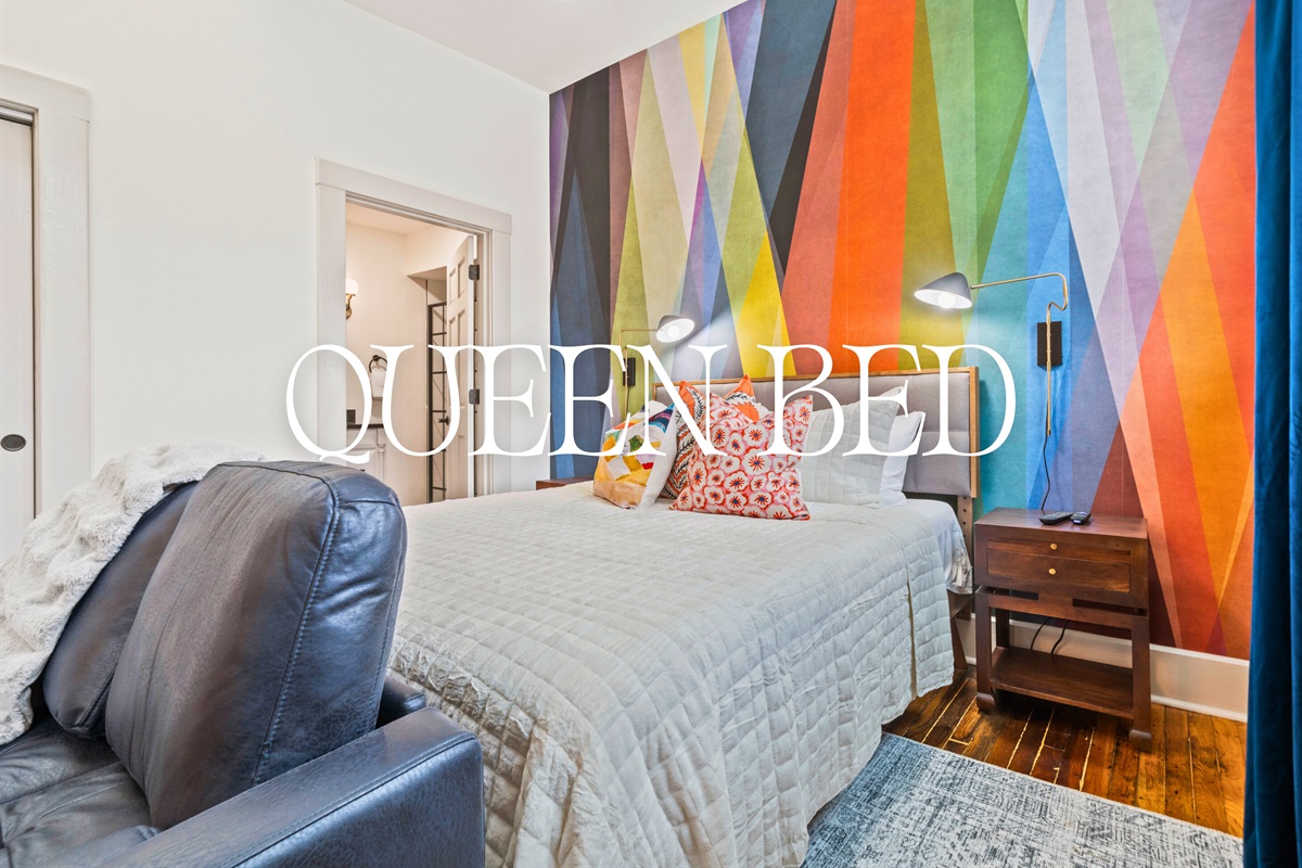 The queen bed is framed by bold wall art and cozy lighting, creating a relaxing space with just the right amount of personality.