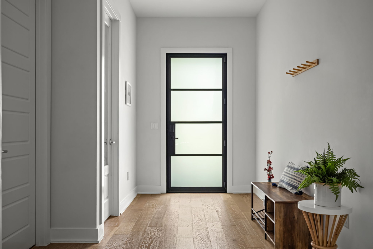 Modern black-framed glass entry door flooded with natural light, paired with a chic console table and greenery for a fresh first impression