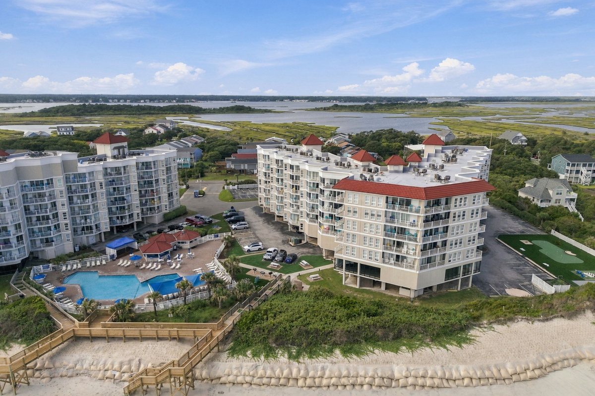 Aerial shot highlighting the beachfront resort complex, outdoor pool area, and surrounding landscape.