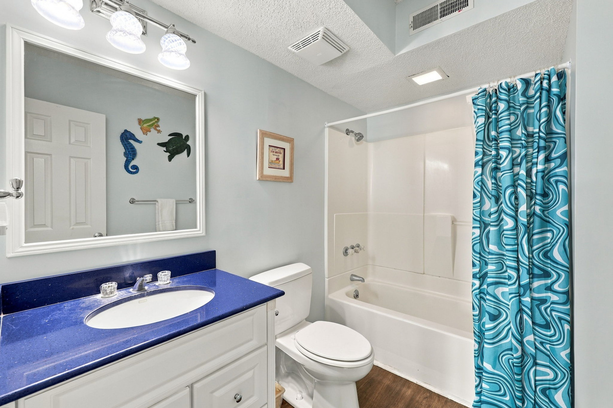 Bright bathroom with a vibrant blue vanity, large mirror, and shower-tub combo.