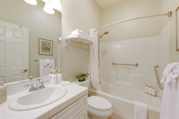 Full bathroom with tub/shower combo, grab bars, mirror, and guest essentials