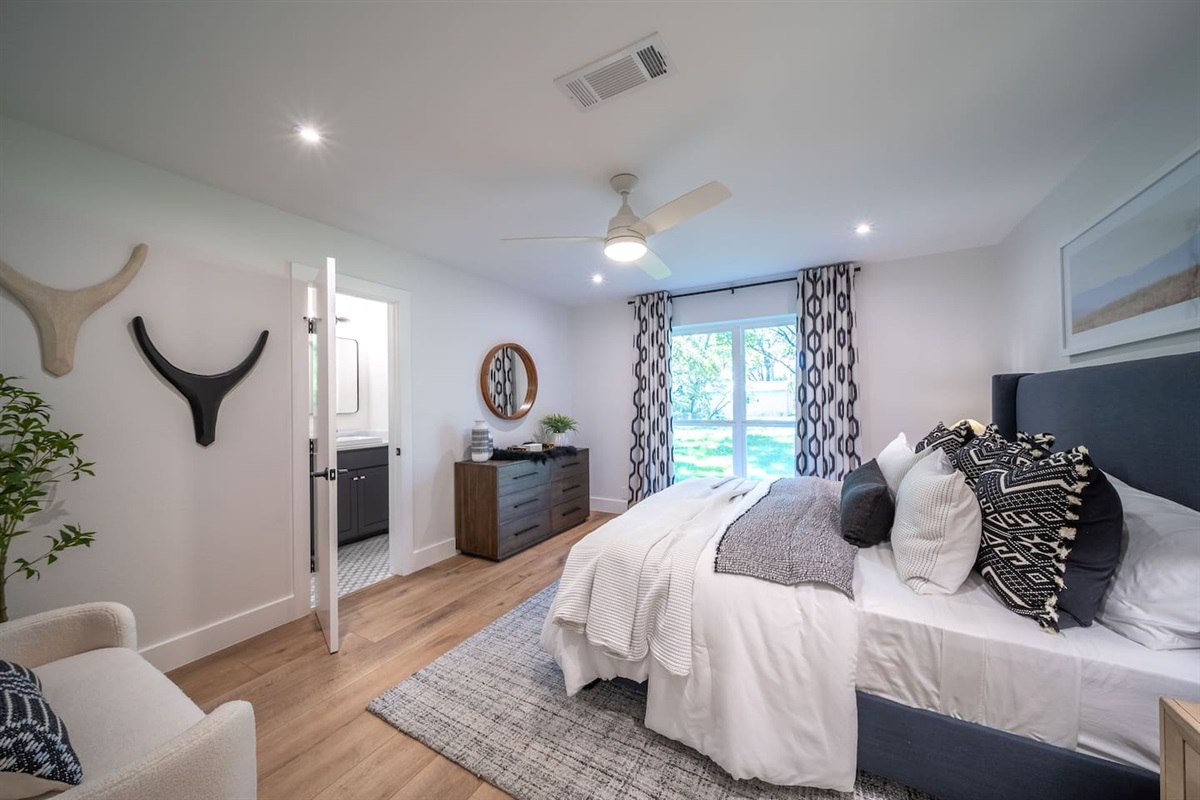 Wide view of Bedroom 2 highlighting the airy layout, soft textiles, and abundant natural light from large windows overlooking the trees. unwind and unpack. Guests enjoy the added benefit of a private ensuite bathroom and a large closet. 