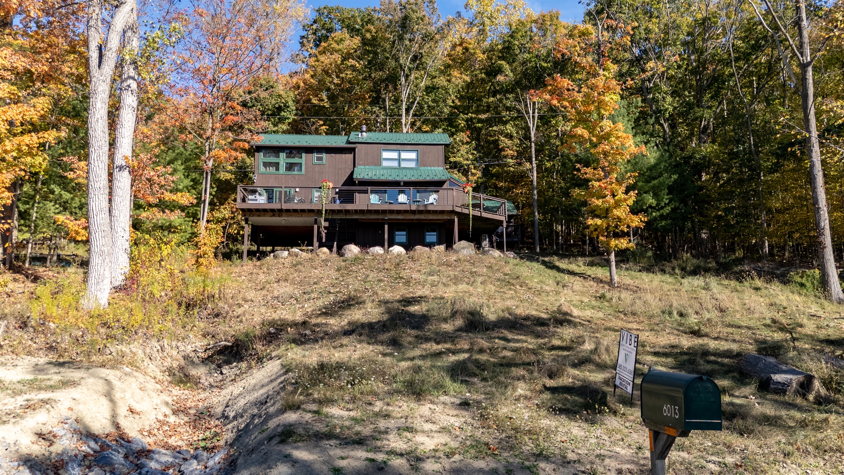 Exterior view of cabin from a hill above showing deck and lakeside proximity.