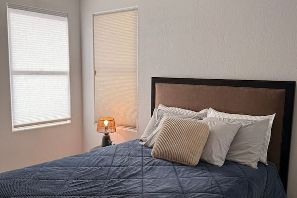 Queen bedroom with ceiling fan, closet storage, side table, and natural light from the corner windows.