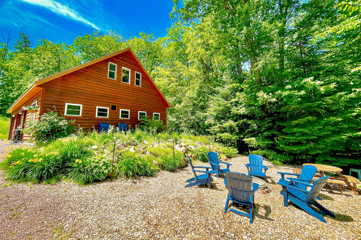 VIew of Rock Garden driving up to property from the road- in the summer  Showing perennial garden fire pit with provided wood and picnic table 