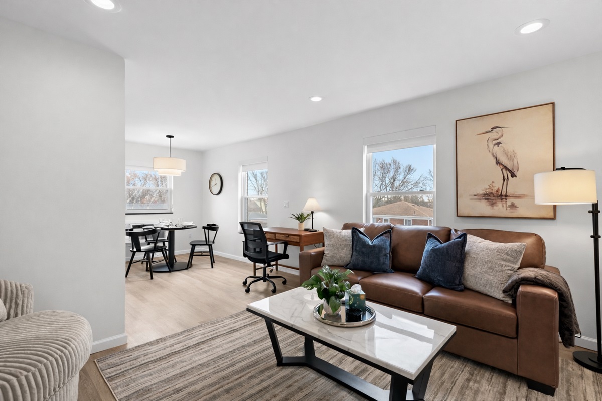 Bright, open living area with plush seating, natural light, and a dedicated workspace—perfect for relaxing, working, or enjoying meals together.
