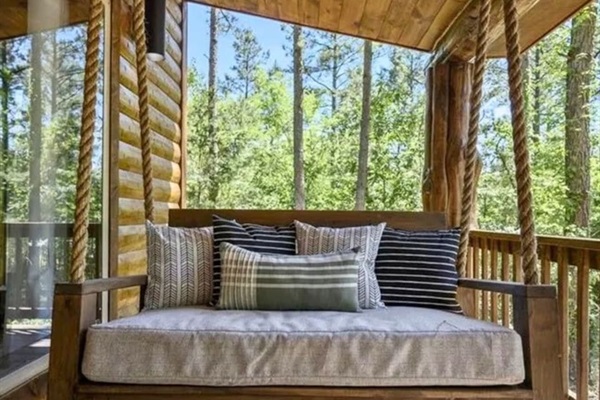 Unwind on the cozy bedded swing under the covered porch, perfect for relaxing afternoons and enjoying peaceful forest views