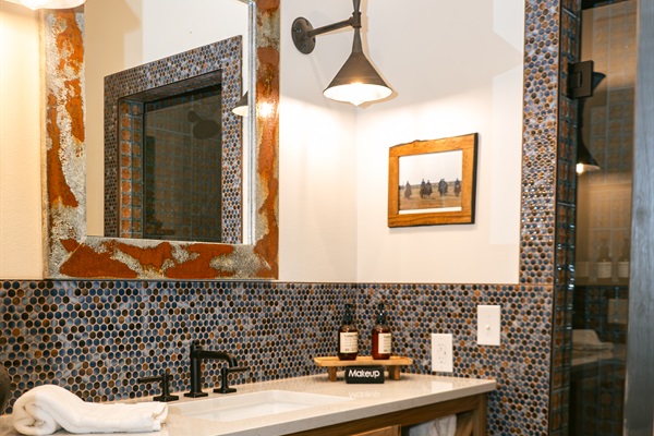 Bathroom #1 at Cutter's Quarters &mdash; Hill Country mosaic tile, a designer sconce, and curated Western art alongside the first king bedroom.