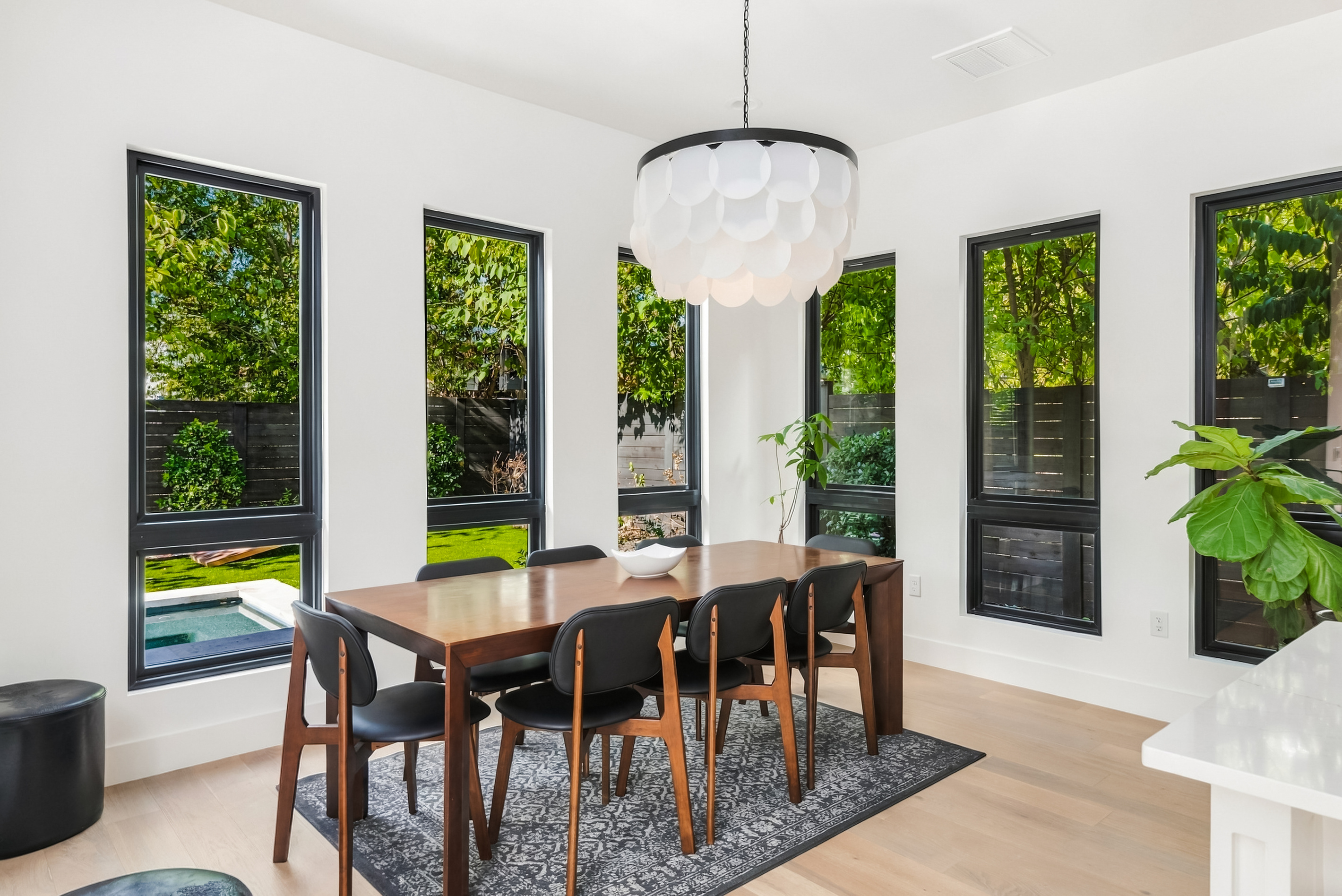 Wood dining table framed by floor-to-ceiling windows and lush greenery.
