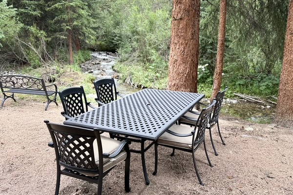 Outdoor dining feels different when the table sits beneath towering trees beside a flowing mountain creek.