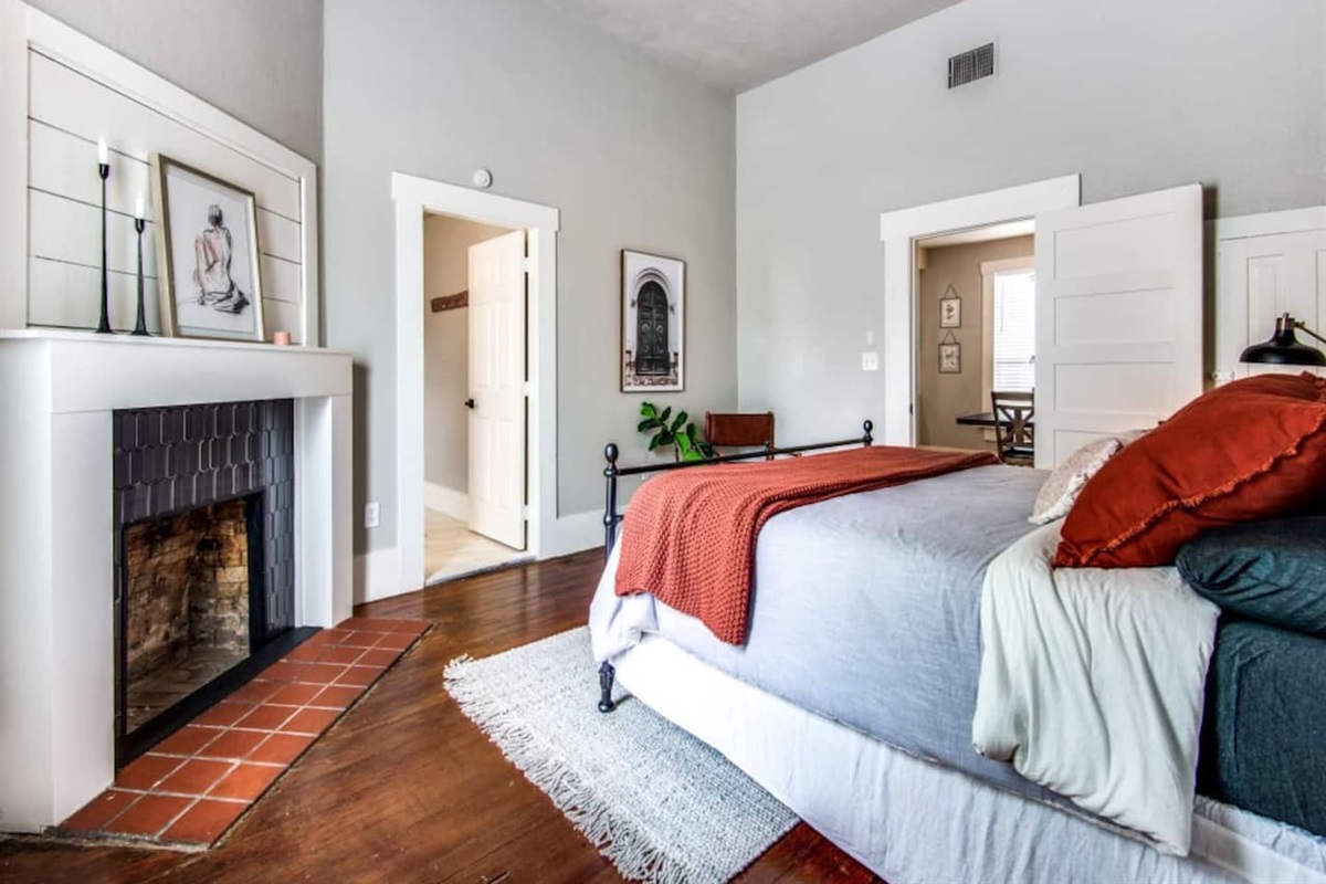 Full layout view of the king suite showing hardwood floors, decorative brick fireplace, ensuite entry, and ceiling fan. Spacious and bright in this renovated modern farmhouse in historic downtown Aubrey TX near Frisco and Denton.