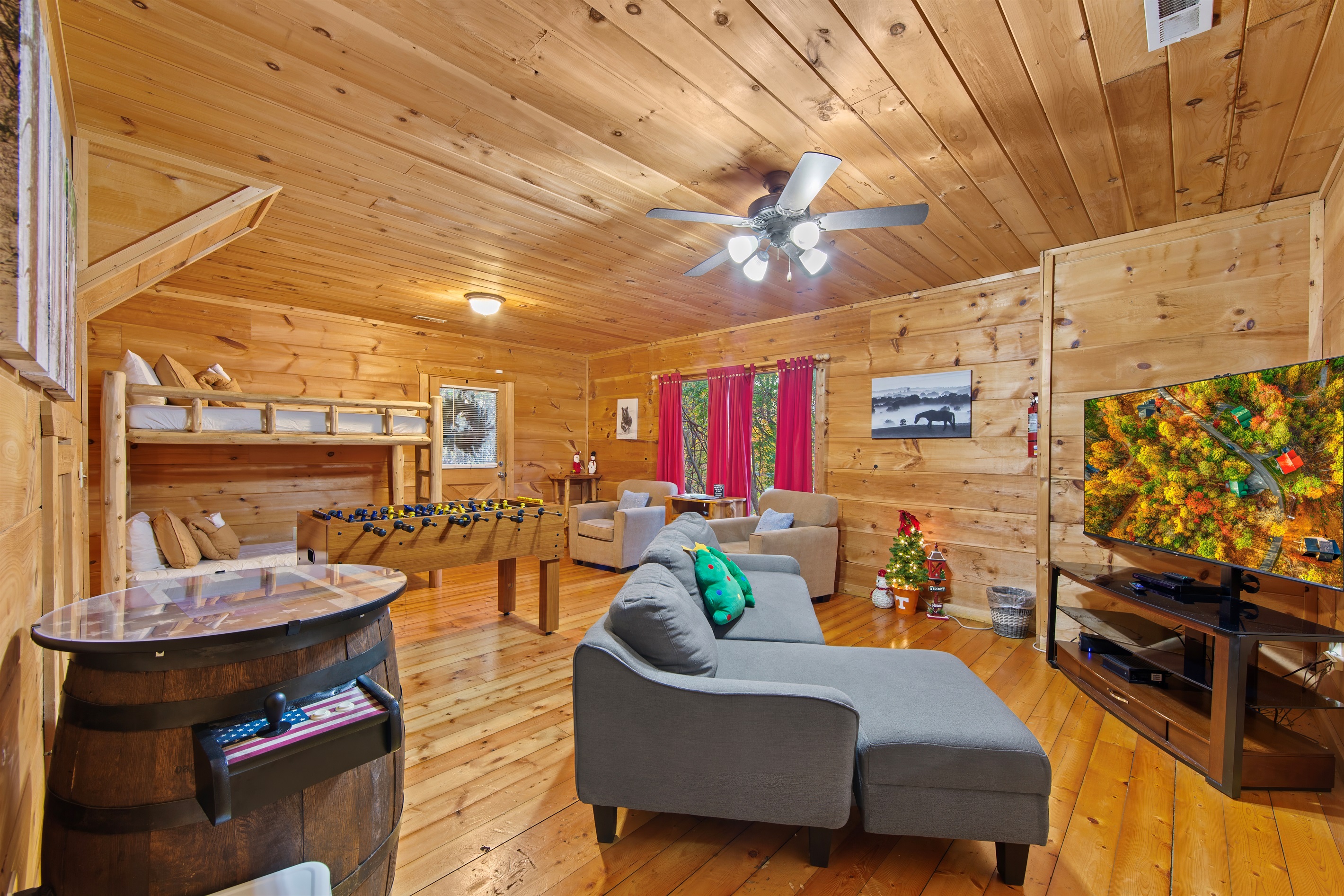 This inviting recreation room features a sectional sofa, a foosball table, and bunk beds, perfect for entertaining or relaxing. Warm wood tones and holiday accents create a cozy, welcoming vibe.